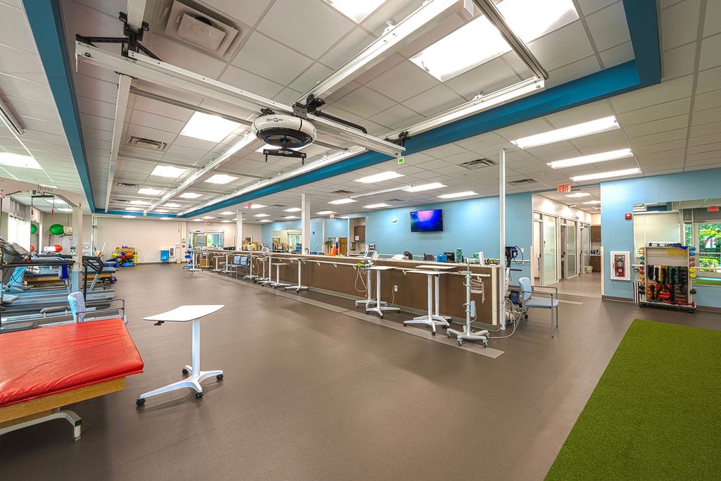 Modern physical therapy gym with exercise equipment, parallel bars, blue walls, and bright lighting.